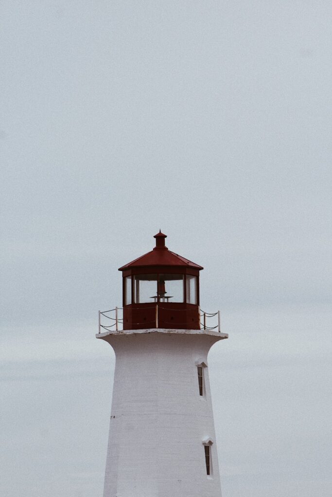 a white lighthouse with a red roof on a cloudy day