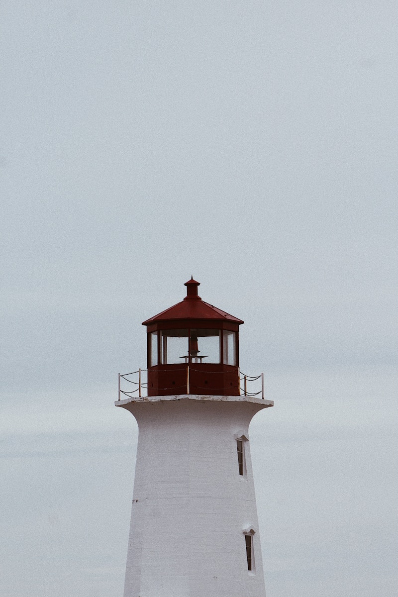 a white lighthouse with a red roof on a cloudy day