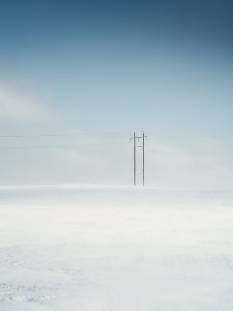 black electric post on snow covered ground under blue sky during daytime