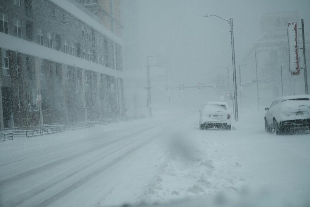 a couple of cars driving down a snow covered street