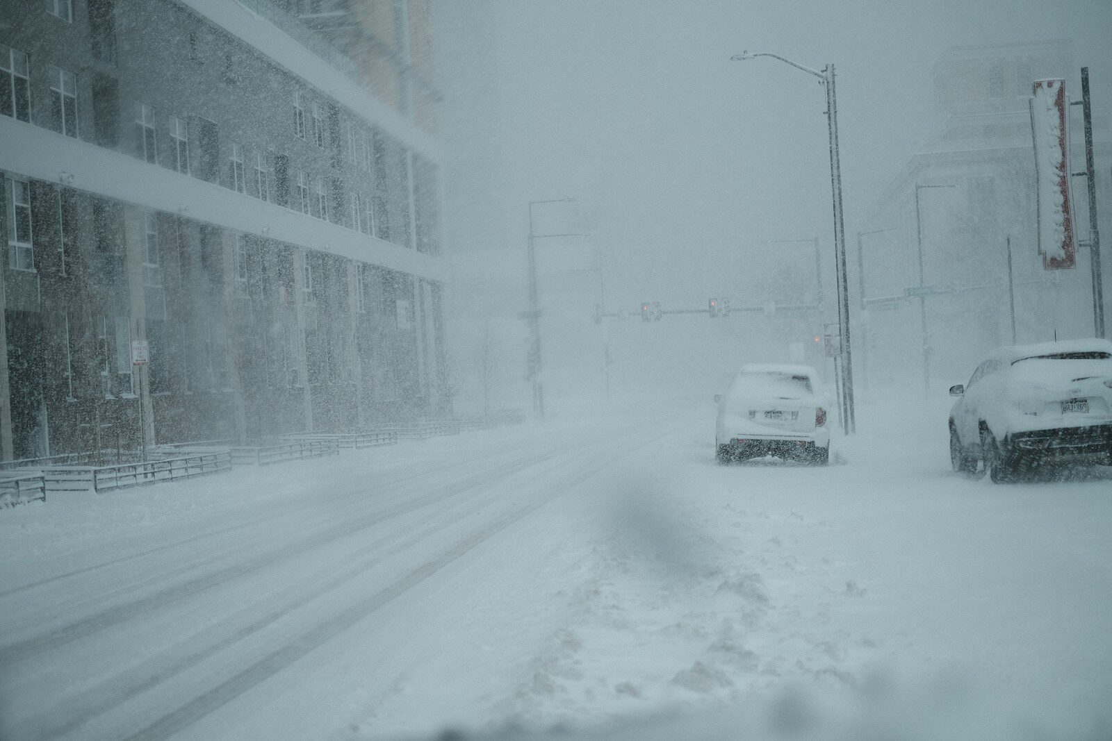 a couple of cars driving down a snow covered street